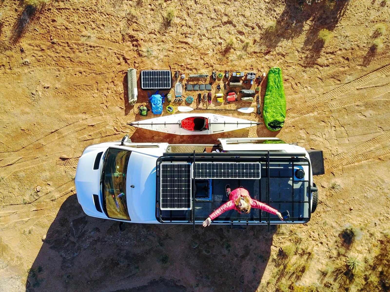 Aerial view of Alaina's first Sprinter van with her standing on the roof showing the solar panels, roof racks, and all her gear organized outside the van