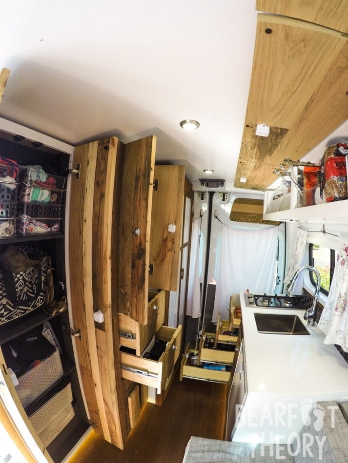 Interior view toward the back of Alaina's first converted Sprinter camper van showing all the storage including floor to cieling cabinets, overhead cabinets, and drawers
