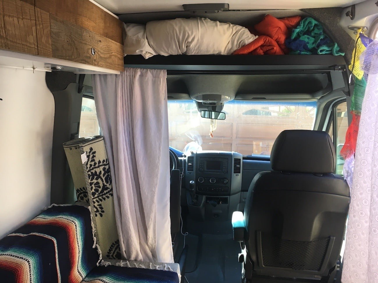 Interior view towards the front of Alaina's first Sprinter camper van showing the driver and passenger deats and a raised headliner shelft above for storage 