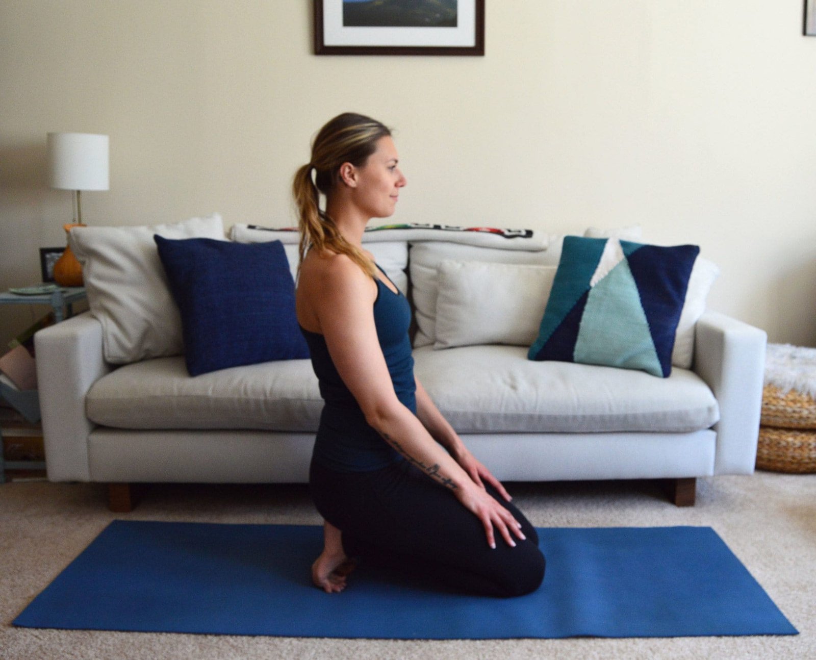 A woman sits back on her heels on her yoga mat at home
