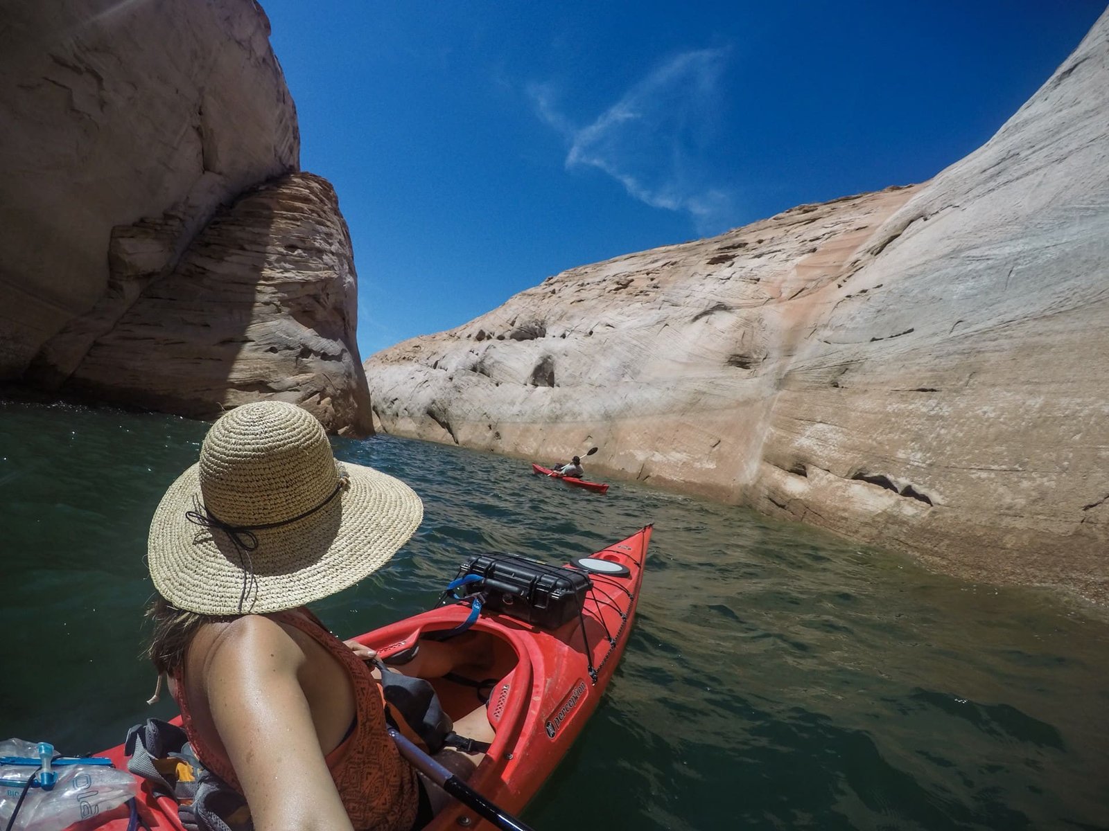 A woman takes a selfie from behind while in a red kayak. She is kayaking in a canyon and wearing a sun hat.
