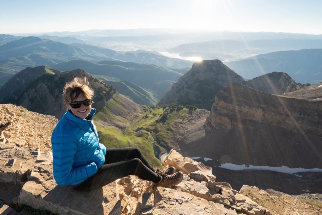 Woman sitting on summit of Mount Timpanogos in Utah with beautiful mountain ridge vista behind her