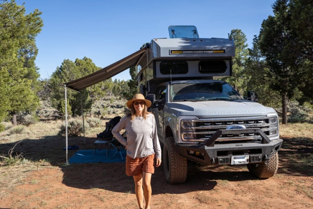 Alaina Hermiston standing next to a Rossmonster Baja Trail adventure truck camper at a desert campsite