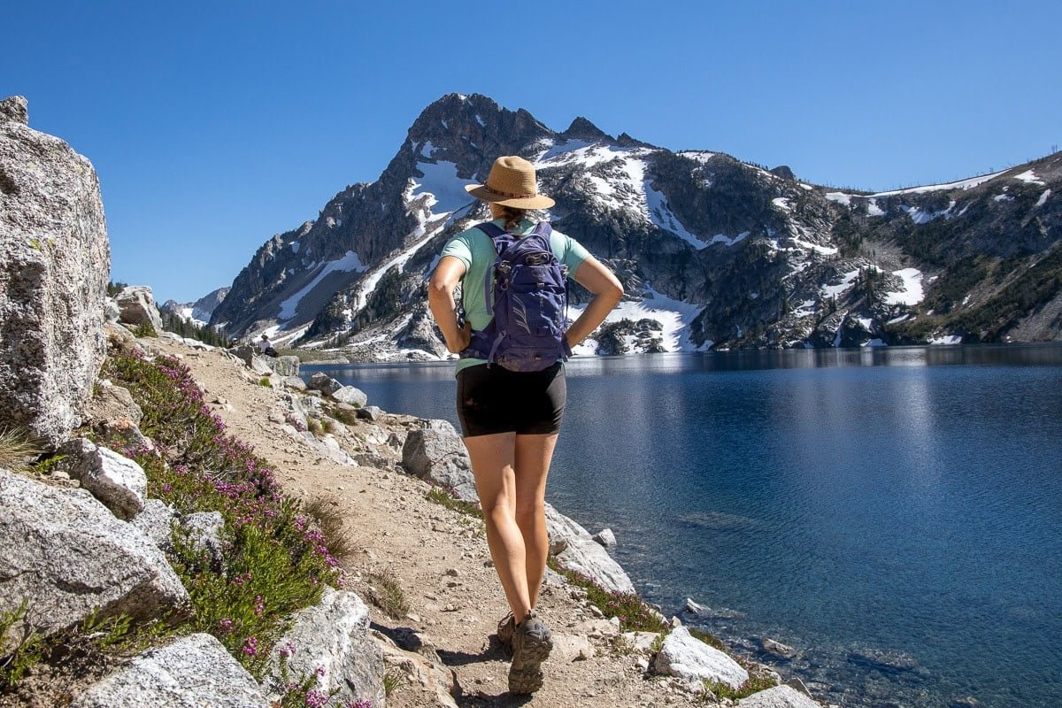 Alaina Hermiston hiking next to a blue alpine lake wearing the Osprey Raven 10 backpack in purple