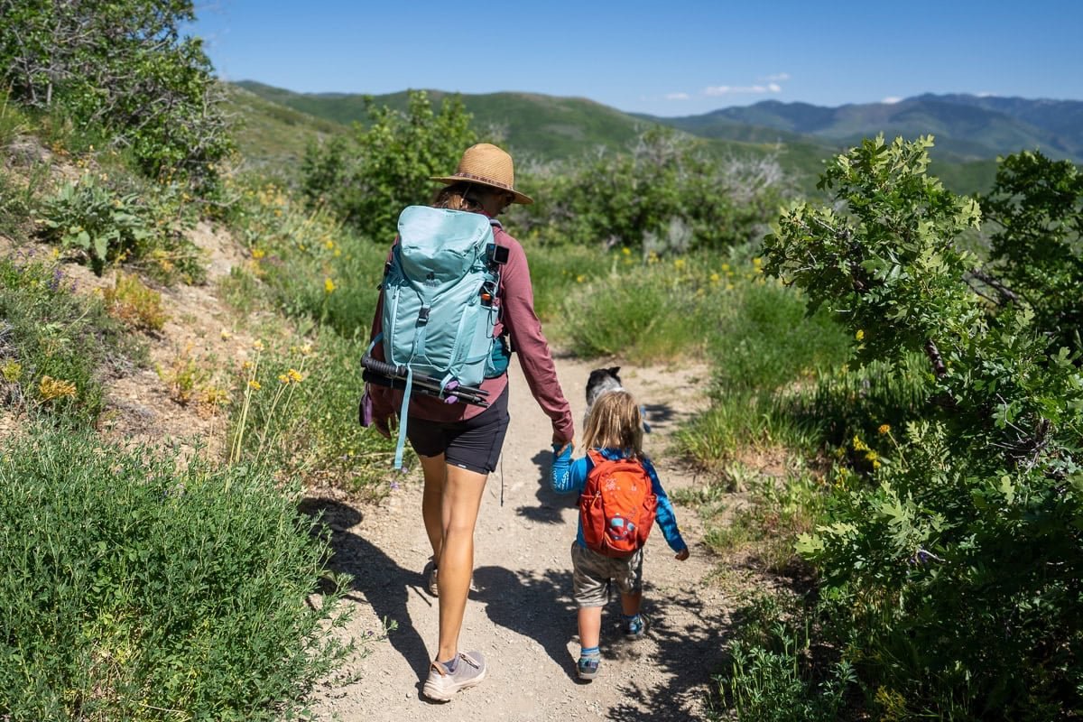 Alaina Hermiston wearing the Deuter Trail 28 SL backpack on a trail in Park City with green foliage next to her 2 year old son