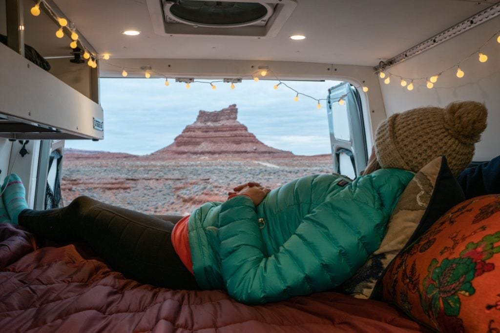 Alaina Hermiston lying in the back of a Sprinter van on the bed with red rocks background