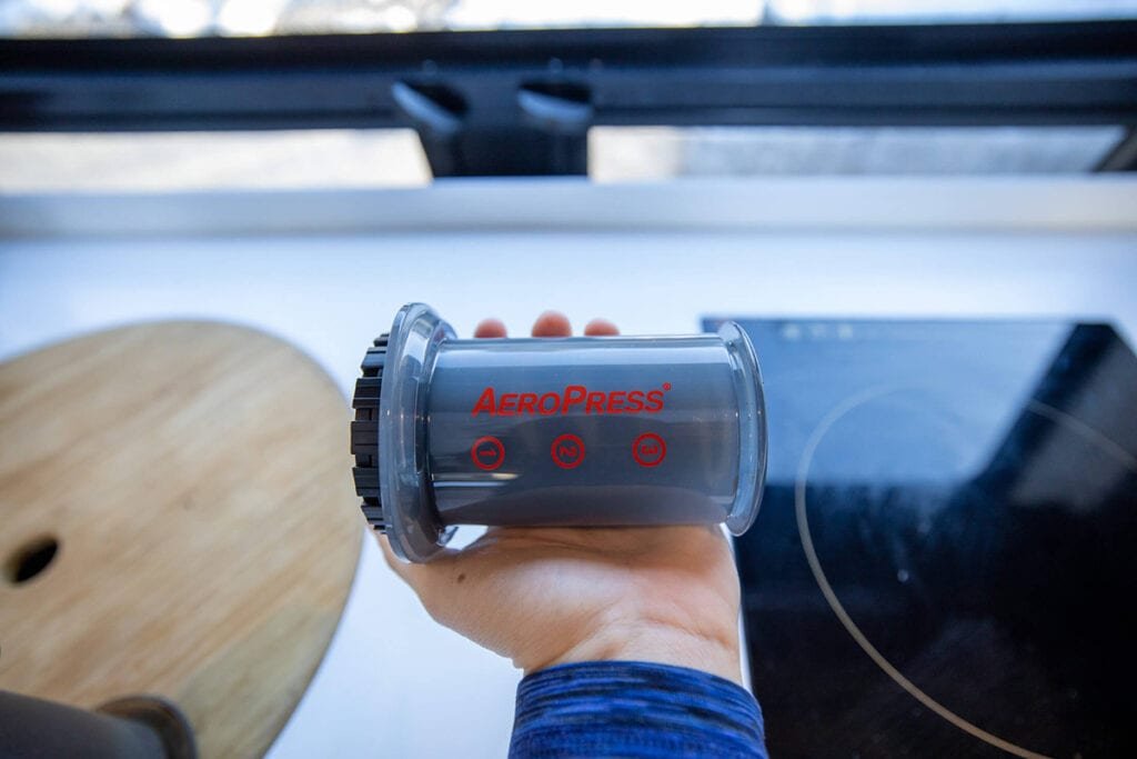 The travel AeroPress Go being held in a palm of someone's hand with an induction stove in the background