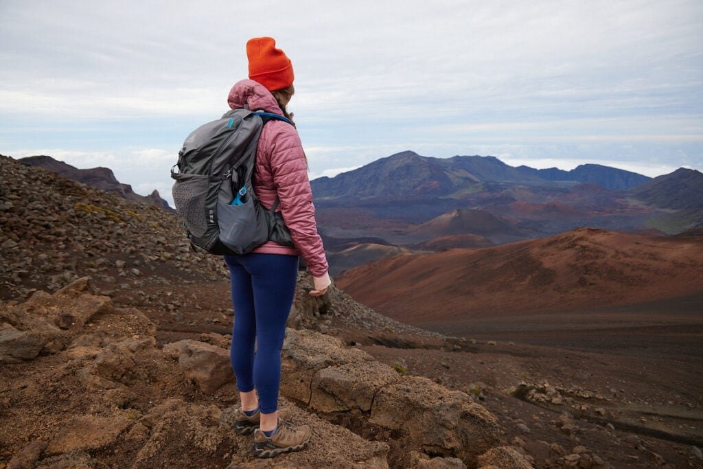 A woman wearing a pink Patagonia Nano Puff Insulated Hoodie on top of Sliding Sands Overlook in Haleakala National Park in Hawaii