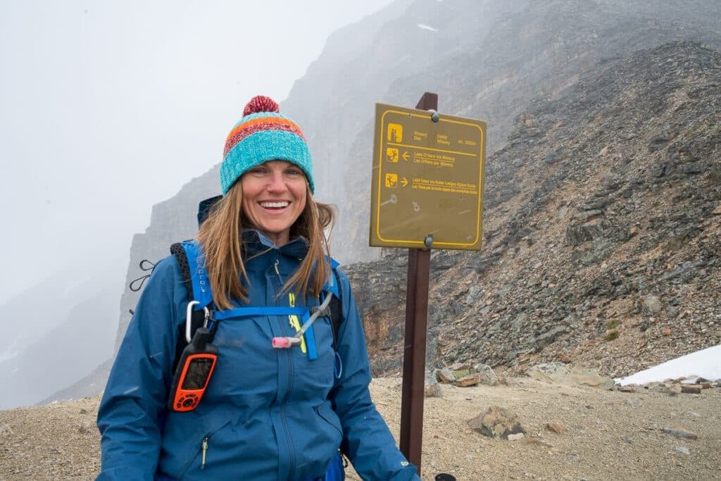 Terrain Spark founder Alaina Hermiston hiking on a foggy rainy day at Lake O'Hara. She is standing next to a trail sign.