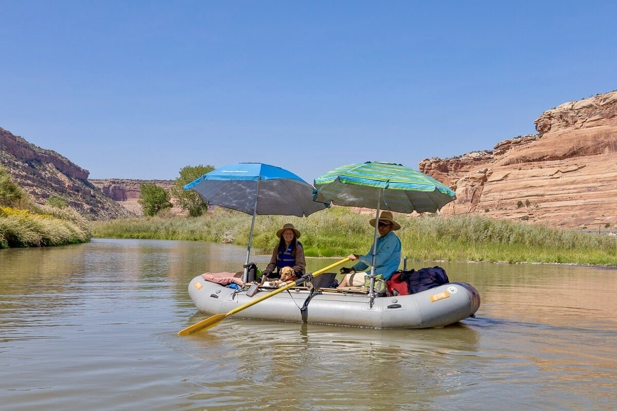 Two people in packraft on the Colorado River in Utah with two umbrellas providing shade