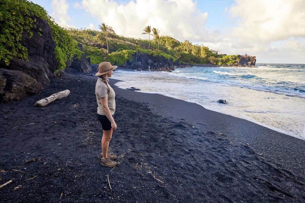 Alaina standing on black sand beach on Maui looking out at ocean
