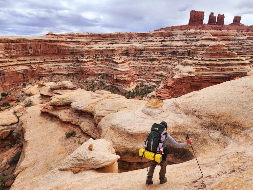 A man wearing a backpacking backpack and carrying trekking poles descends through the Chocolate Drops in the Maze district, Canyonlands National Park