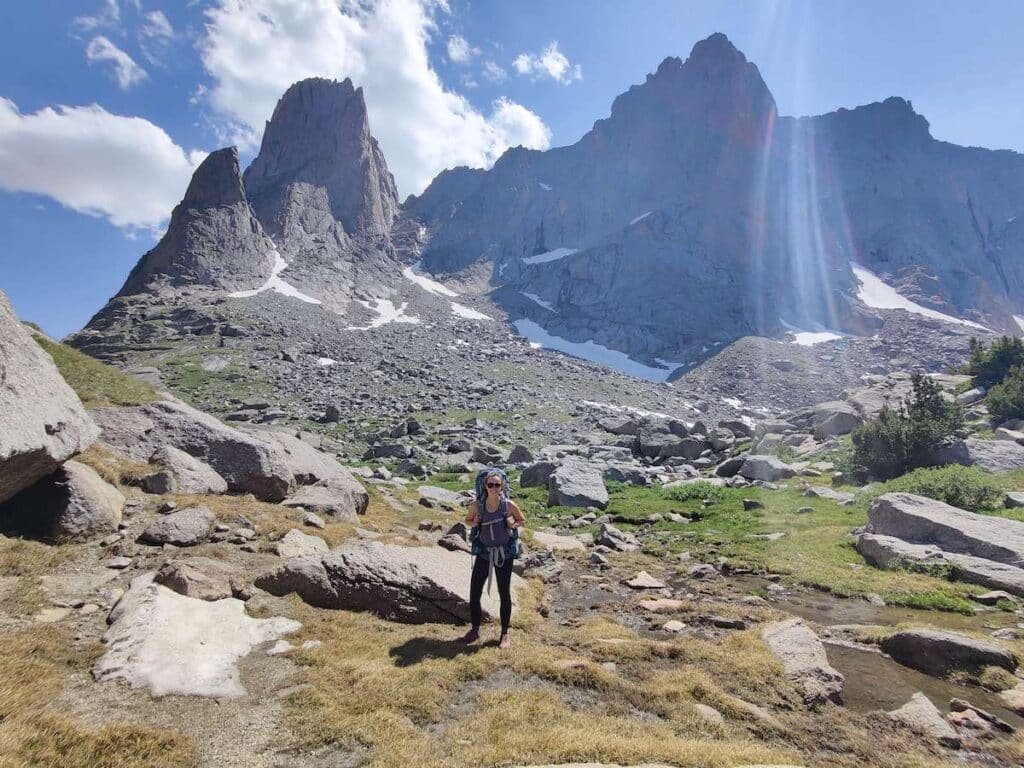 Female backpacker smiling for photo in Cirque of the Towers region of Wind River Gorge in Wyoming with tall mountain peaks behind her