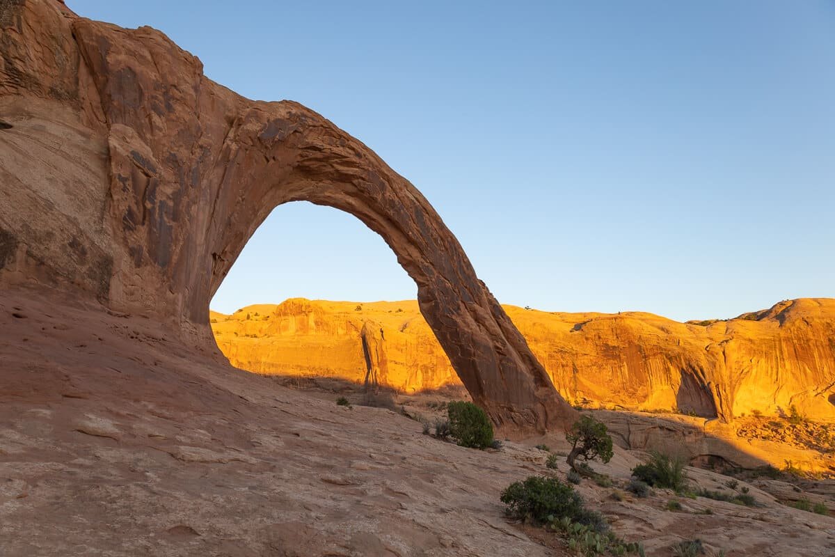 Corona Arch in Moab with sun casting a glow over rock bluffs in the background
