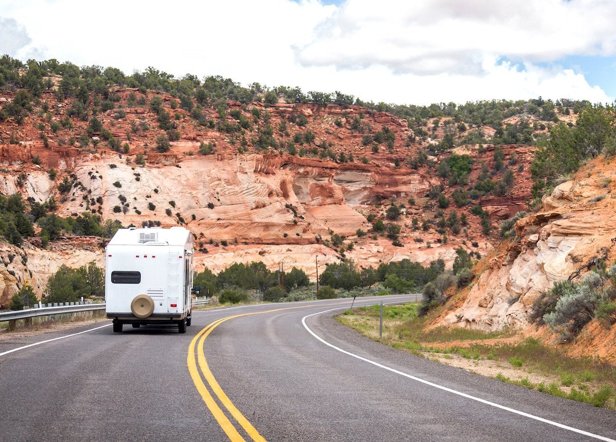 A white camper driving along the highway near Bryce Canyon National Park with red rock formations on both sides.