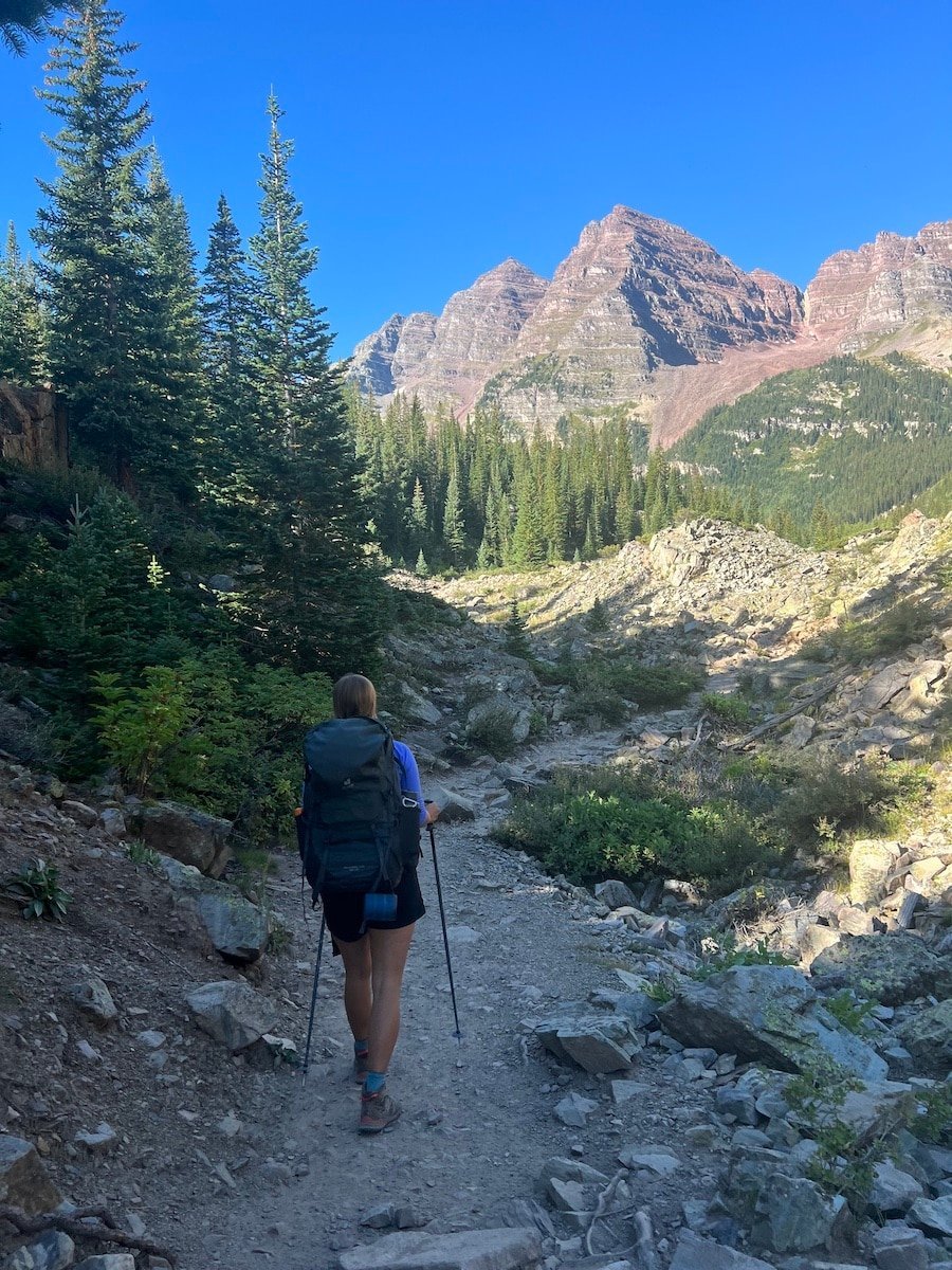The back of a female hiker with a backpack on hiking towards one of the peaks in the Maroon Bells