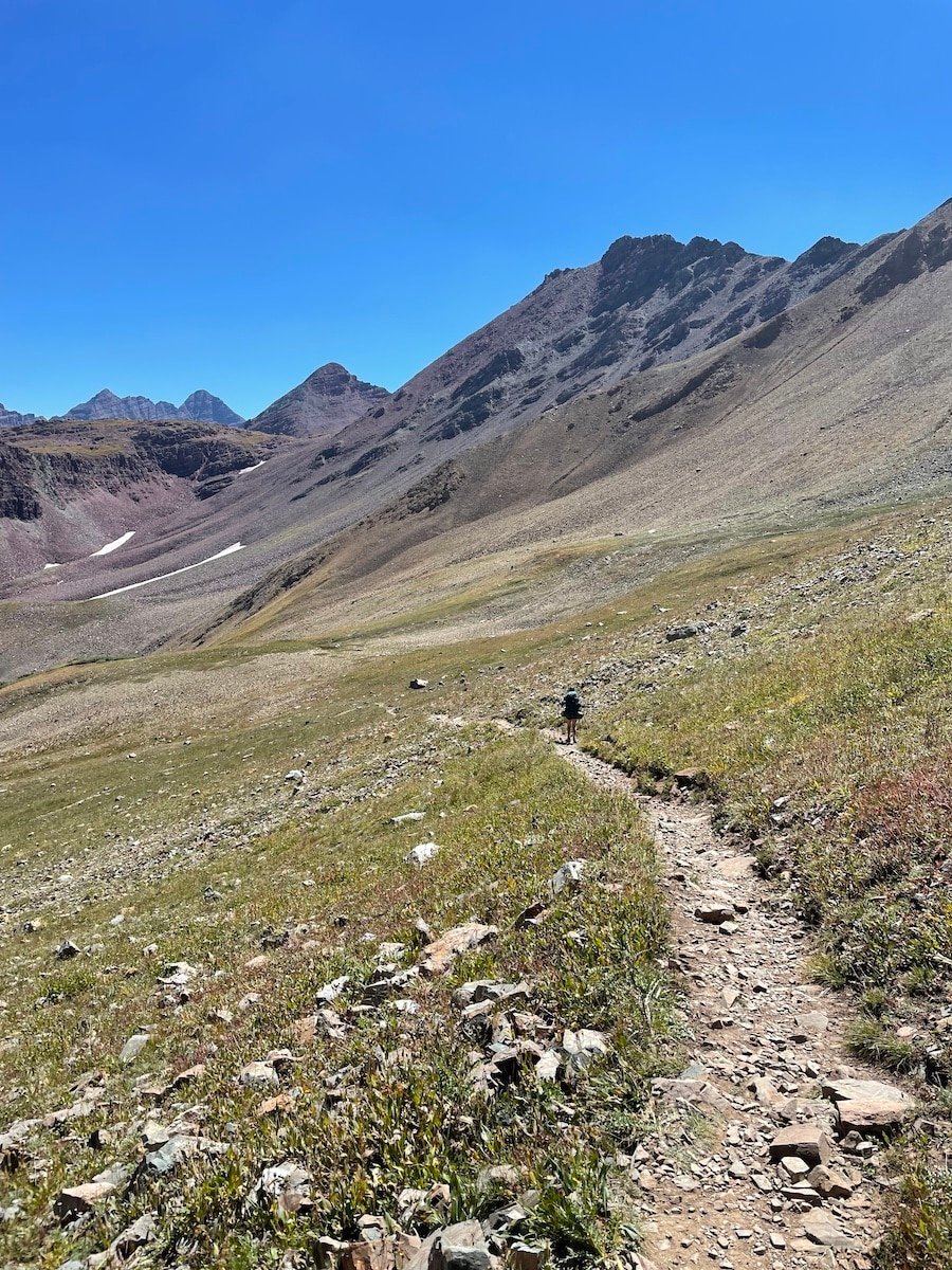 Hiker descending Trail Rider Pass on the Four Pass Loop with rocks on the trail and mountain peaks in the distance
