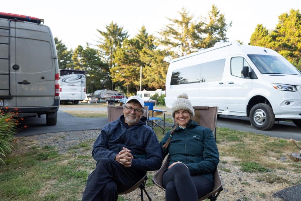 Terrain Spark founder Alaina Hermiston sitting in a camp chair next to her dad at a campsite with their Sprinter vans behind them