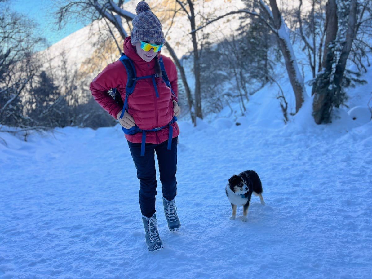 Terrain Spark founder Alaina Hermiston winter hiking with her mini aussie dog on a snowy trail in Utah