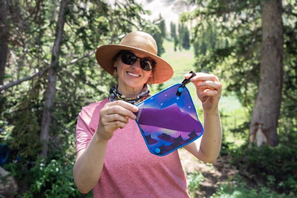 Alaina Hermiston holding Kula Cloth pee rag featuring a bear next to a lake with a cosmic mountain scene