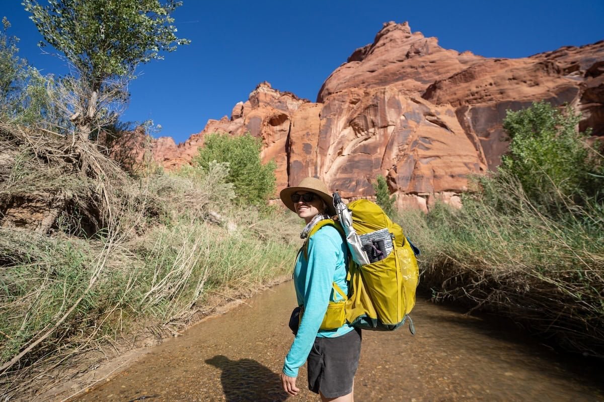 Alaina Hermiston standing in a river in Paria Canyon with a backpacking pack on