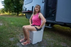 Alaina Hermiston demonstrating how to use the Compocloset Cuddy Lite composting toilet standing in front of a truck camper
